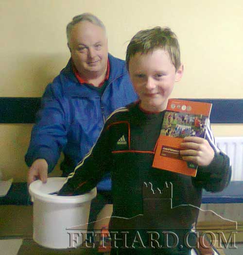 Cathal Ryan, holding the current GAA's Code of Behaviour booklet, drawing the winning name in the Juvenile Membership Draw, under the watchful eye of Club Chairman, Patsy Lawrence.